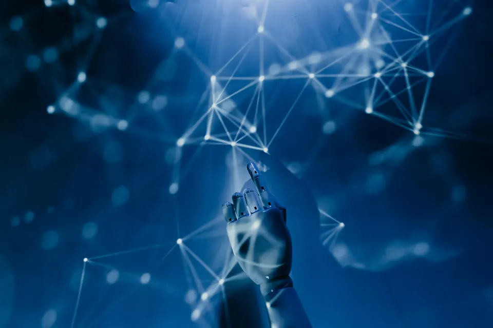 A robotic hand reaching up to touch a glowing network of connected nodes, representing artificial intelligence and connected systems